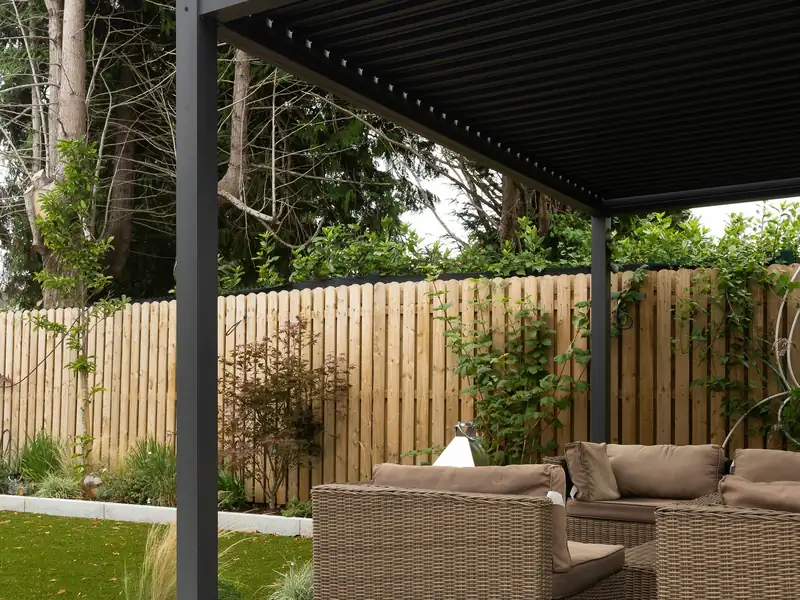 Pergola bioclimatique en aluminium anthracite à lames orientables au-dessus d’un salon de jardin sur terrasse dallée