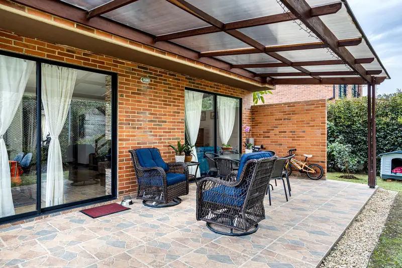 Couverture de terrasse adossée à toit incliné translucide sur structure métallique brune devant une maison en briques