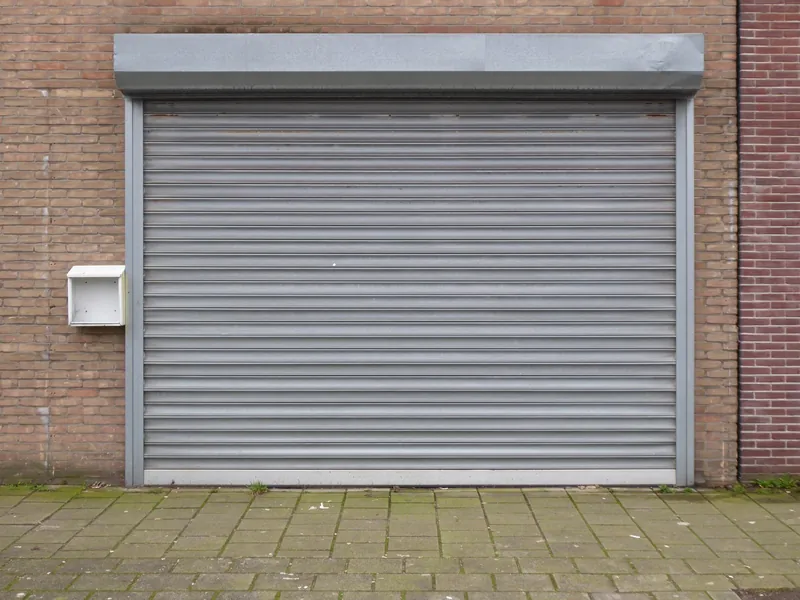 Porte de garage enroulable à lames grises avec son coffre, dans une façade en briques