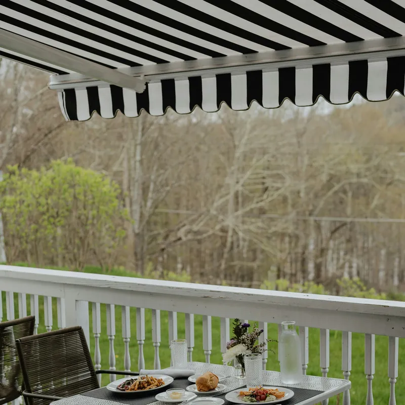 Store banne à rayures noires et blanches déployé au-dessus d’une terrasse en bois avec table dressée