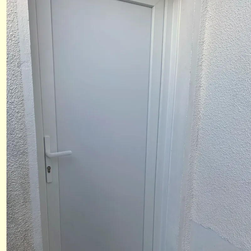 Porte PVC blanche pleine posée dans une ouverture de mur crépi blanc